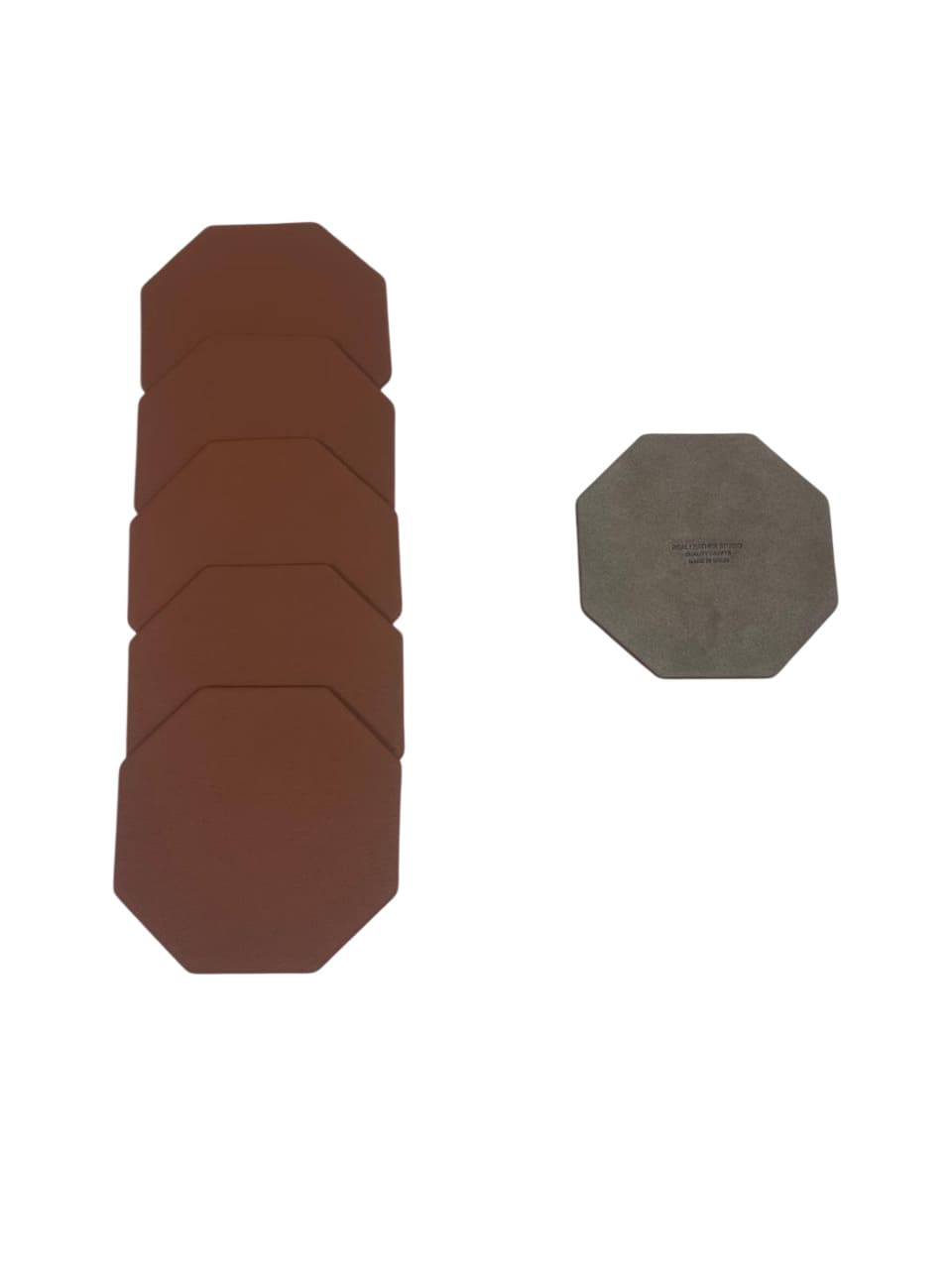 Detalle de un set de posavasos octogonales de piel apilados junto a una unidad que muestra el reverso grabado.