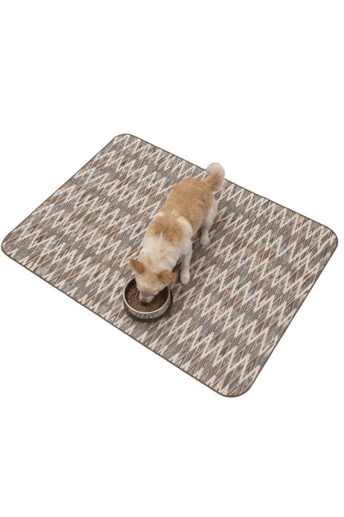 Dog eating from a bowl on an ethnic design pet food mat that keeps the feeding area clean.